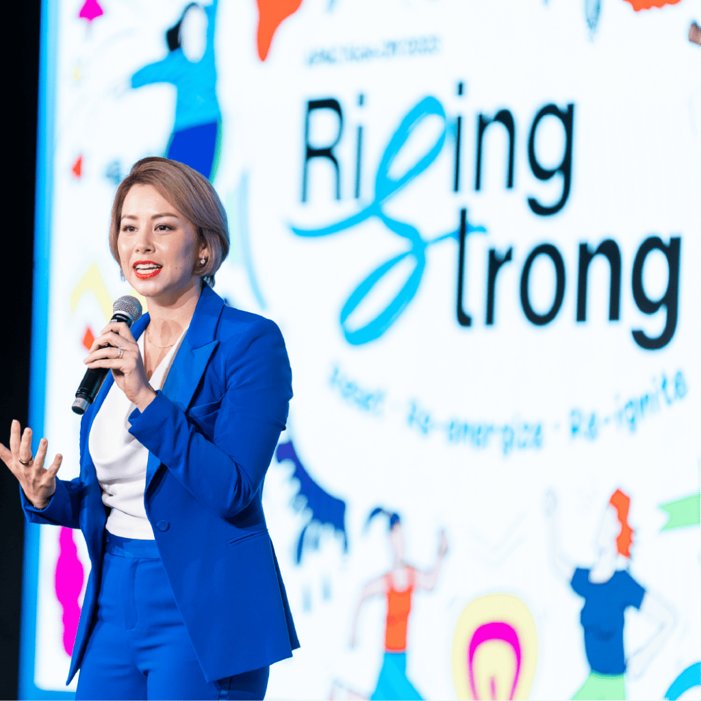 Female speaker in a vibrant blue pantsuit addresses an audience during a 'Rising Strong' event, showcasing professional corporate event planning