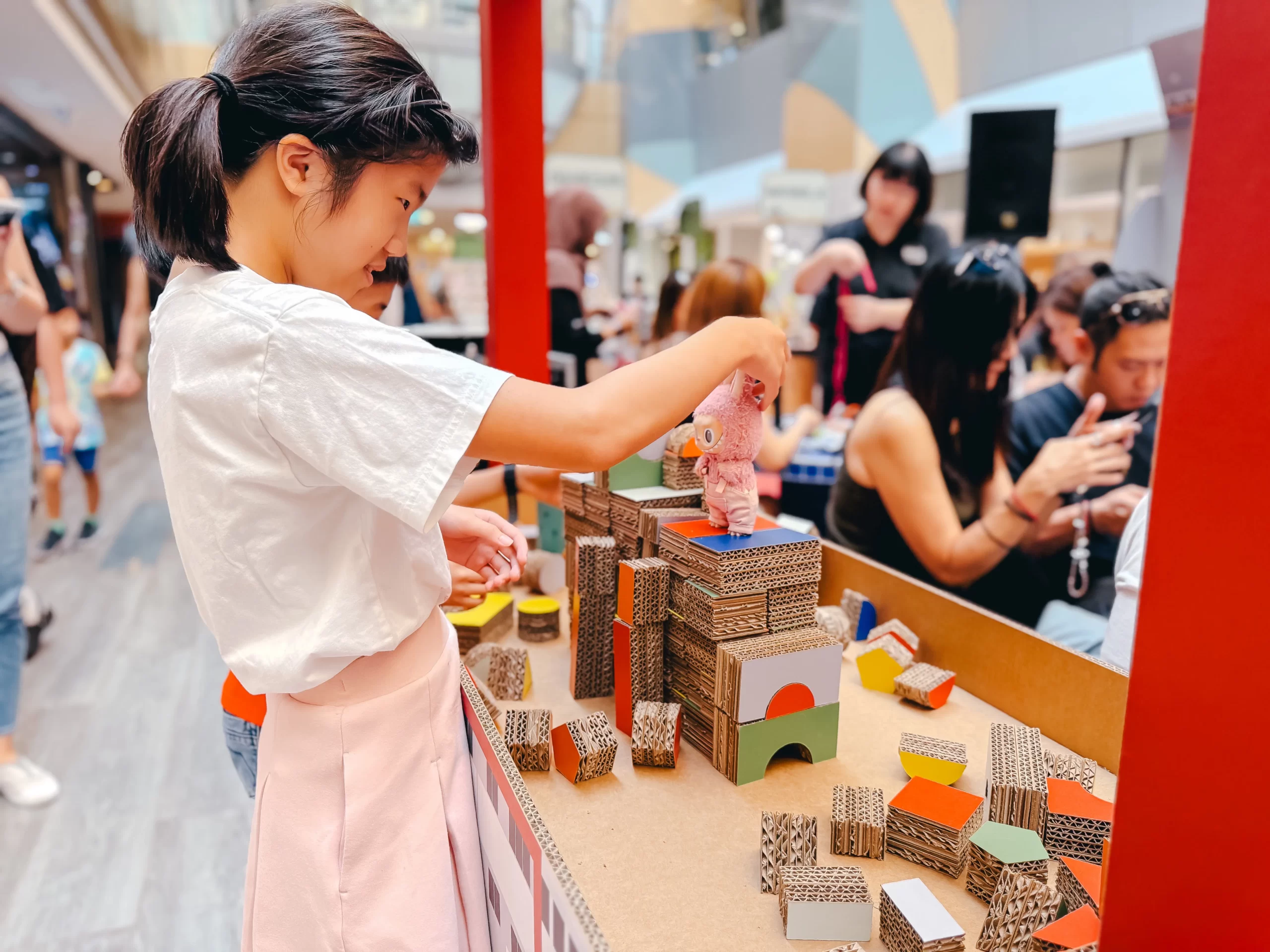 A young girl engaging in a creative cardboard building workshop during a sustainable brand activation event in a shopping mall.