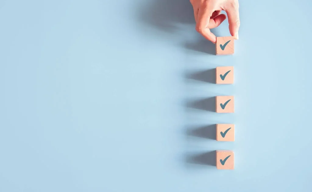 A hand placing the top wooden block onto a vertical stack of five blocks, each marked with a checkmark, symbolizing a step-by-step guide to choosing the right company event management partner.