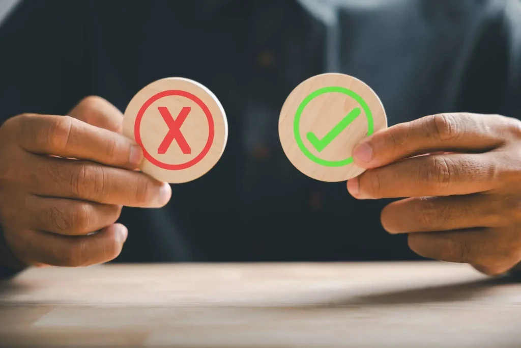 A person holding two wooden discs — one with a red X mark and one with a green checkmark — representing the decision-making process of whether outsourcing event management is right for your company