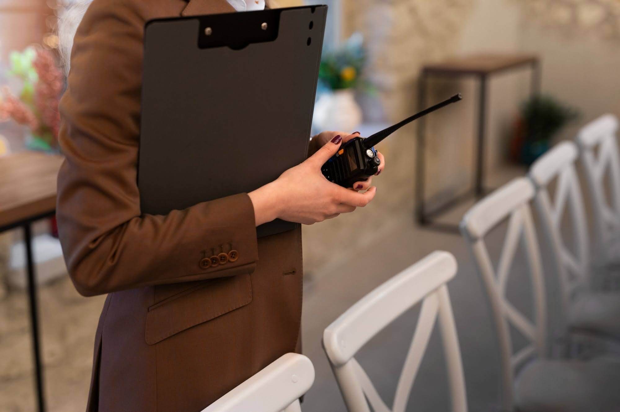 5:05 PM A professional event organizer on-site at a venue, holding a clipboard and walkie-talkie.